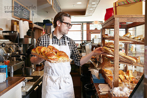 Männlicher Arbeiter in einer Bäckerei  der frisches Gebäck in eine Vitrine stellt