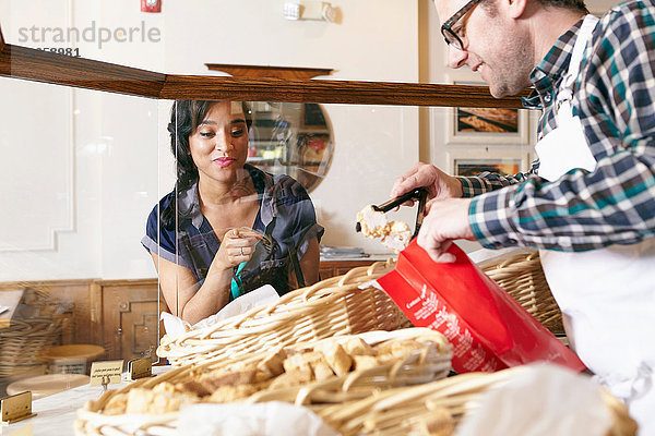 Kunde in Bäckerei zeigt auf Backwaren  Arbeiter legt Waren in Tüte