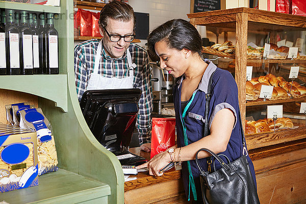 Kunde in Bäckerei  der die Waren mit einem Kartenautomaten bezahlt