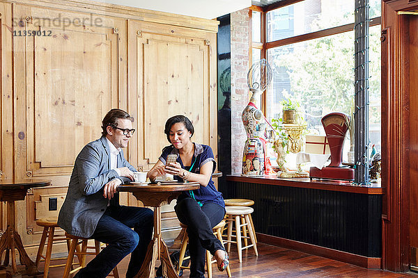 Mann und Frau sitzen in einem Café  trinken Kaffee und schauen auf ein Smartphone