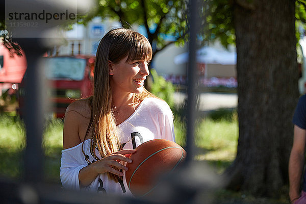 Junge Frau im Freien  Basketball haltend  lächelnd