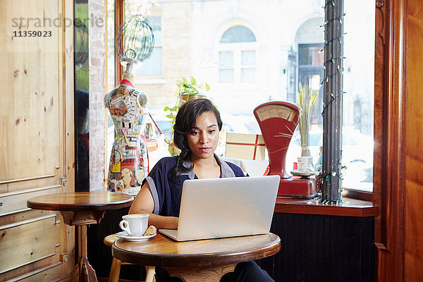 Junge Frau sitzt im Café und benutzt einen Laptop