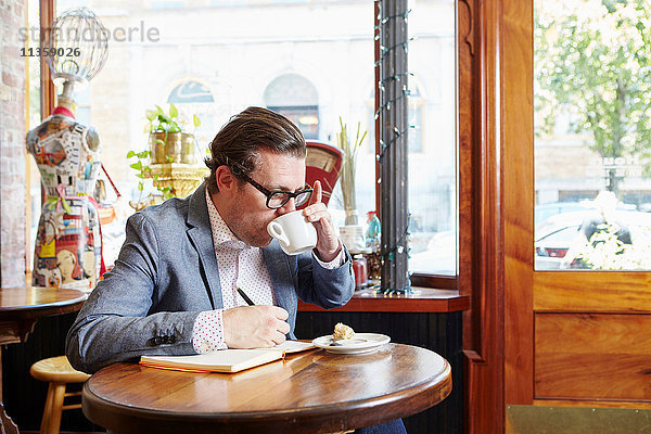 Mann sitzt im Café  trinkt Kaffee  schreibt in ein Notizbuch