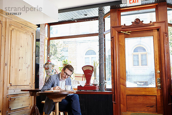 Mann sitzt im Café und schreibt in ein Notizbuch
