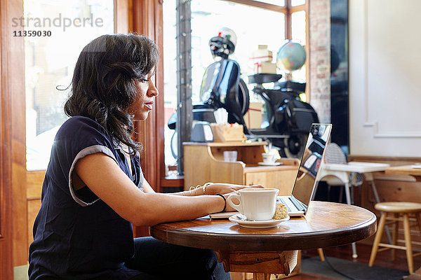 Junge Frau sitzt im Café und benutzt einen Laptop