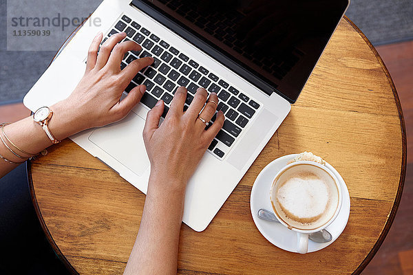 Junge Frau sitzt im Café  benutzt Laptop  Draufsicht