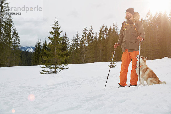 Mittelgroßer erwachsener Mann auf Schneeschuhen  Hund neben ihm  Elmau  Bayern  Deutschland