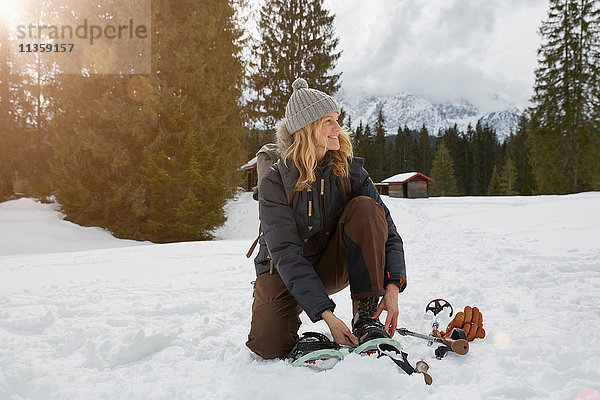 Reife Frau zieht Schneeschuhe in verschneiter Landschaft an  Elmau  Bayern  Deutschland