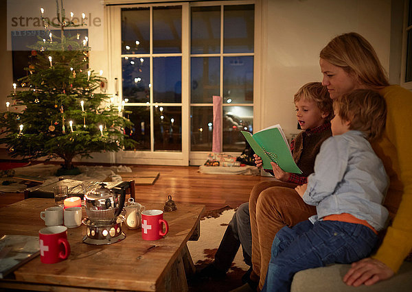 Mutter und Söhne sitzen zu Weihnachten zu Hause und lesen Buch