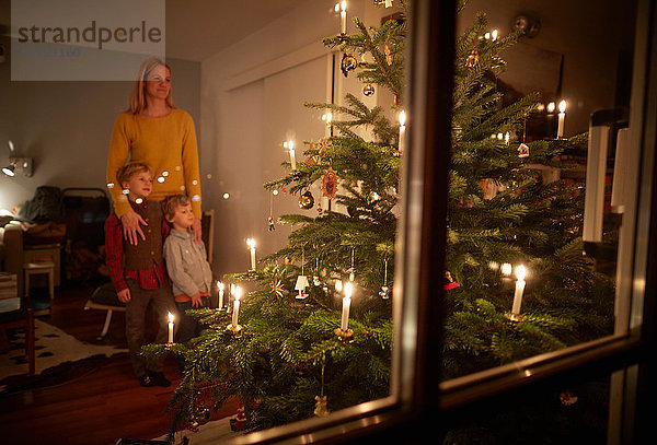 Mutter und Söhne sitzen zu Weihnachten zu Hause und schauen auf den beleuchteten Weihnachtsbaum