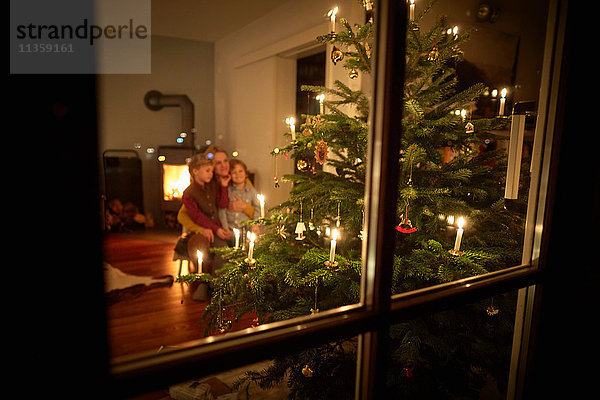 Mutter und Söhne sitzen zu Weihnachten zu Hause und schauen auf den beleuchteten Weihnachtsbaum