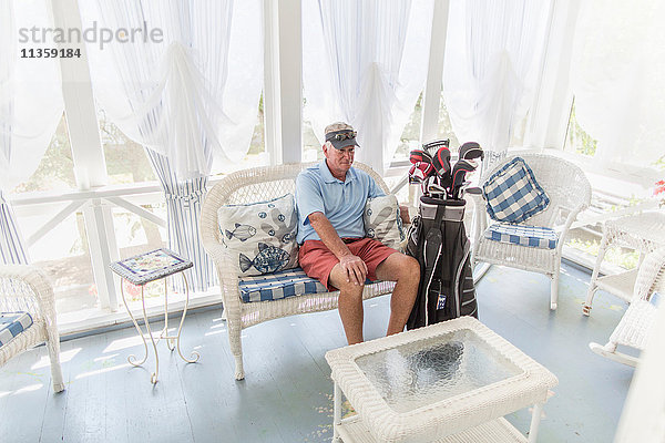 Älterer männlicher Golfspieler sitzt im Wintergarten mit Golftasche