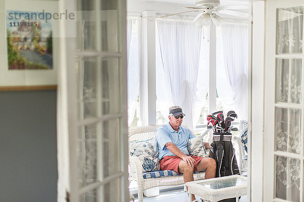Älterer männlicher Golfer  der mit einer Golftasche durch die Tür des Wintergartens sitzt
