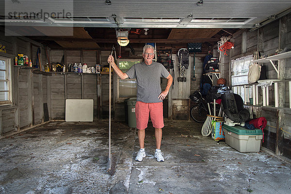 Porträt eines älteren Mannes  der in der Garage steht und einen Besen hält