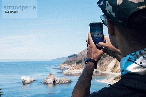 Über-Schulter-Ansicht eines Mannes  der die Küste auf einem Smartphone fotografiert  Big Sur  Kalifornien  USA