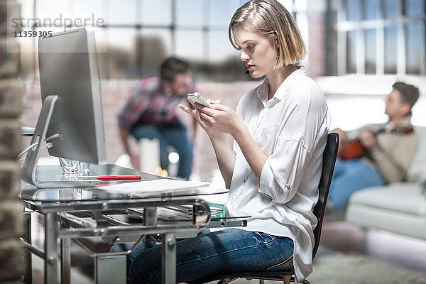Junge Frau zu Hause  am Schreibtisch arbeitend  mit Smartphone