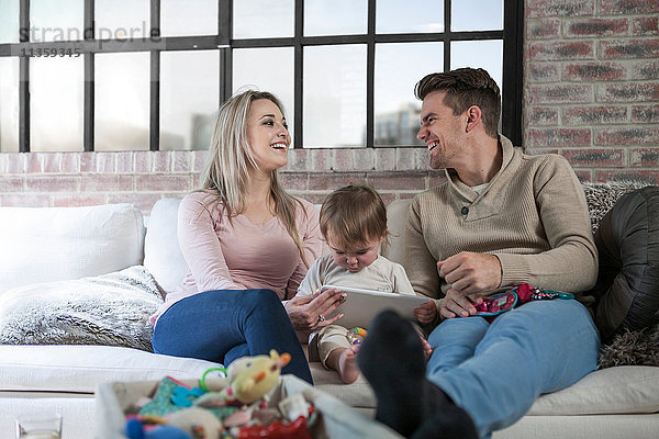 Mutter und Vater sitzen mit Kleinkind auf dem Sofa  Kleinkind hält digitales Tablett