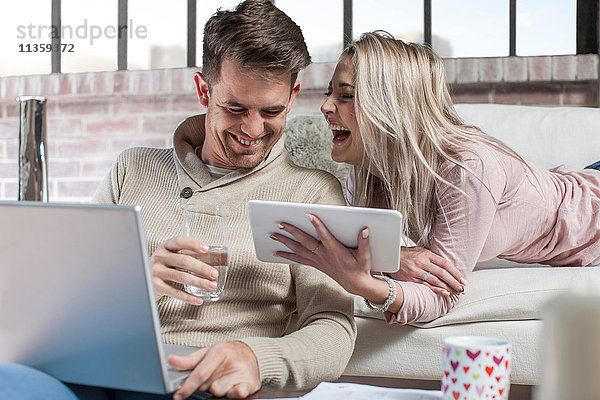 Paar zu Hause  Mann mit Laptop  Frau mit digitalem Tablet  lachend