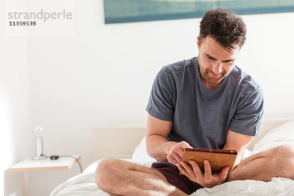 Mann sitzt auf Bett mit digitalem Tablett