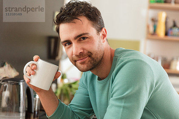 Porträt eines Mannes  der eine Kaffeetasse hält und lächelnd in die Kamera schaut