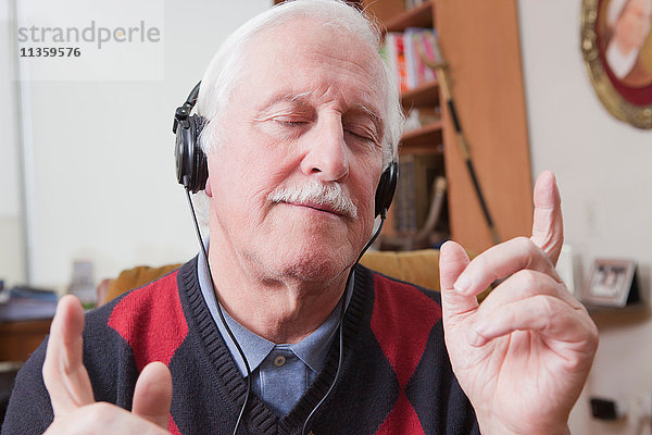 Senior Mann  der zu Hause Musik über Kopfhörer hört.
