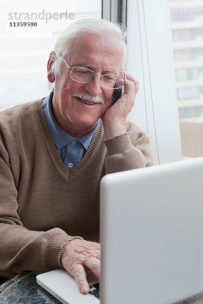 Senior Mann mit Handy und Laptop zu Hause