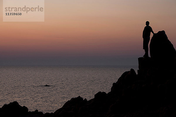 Silhouette eines Mannes auf Felsen mit Blick auf den Ozean bei Sonnenuntergang  Capo Testa  Gallura  Sardinien  Italien