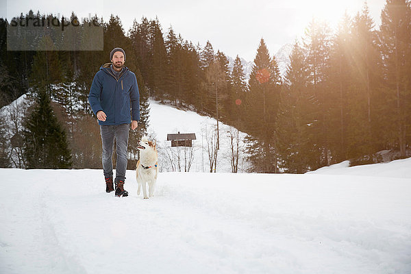 Mann geht mit dem Hund über die verschneite Landschaft  Elmau  Bayern  Deutschland