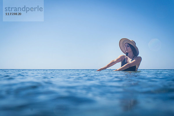 Junge Frau mit Sonnenhut watend im tiefblauen Meer  Villasimius  Sardinien  Italien