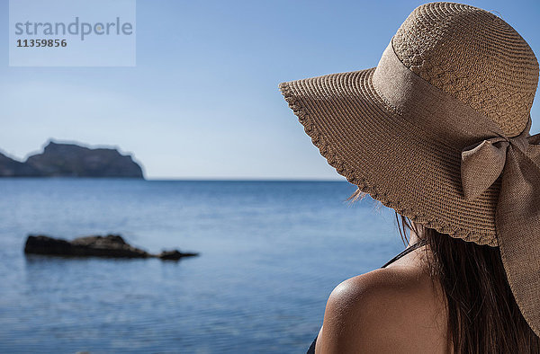 Über-Schulter-Ansicht einer jungen Frau mit Sonnenhut  die aufs Meer hinaussieht  Villasimius  Sardinien  Italien