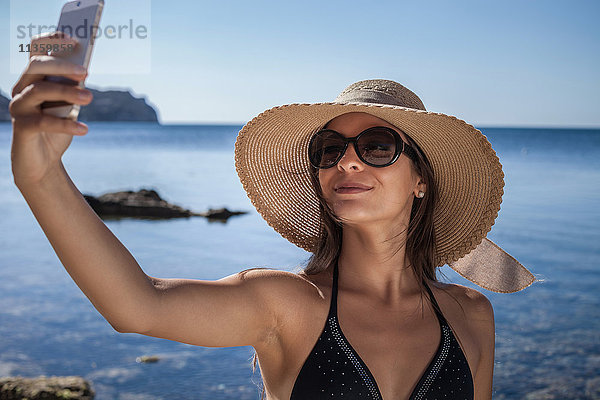 Junge Frau mit Sonnenhut am Strand mit Smartphone-Selfie  Villasimius  Sardinien  Italien