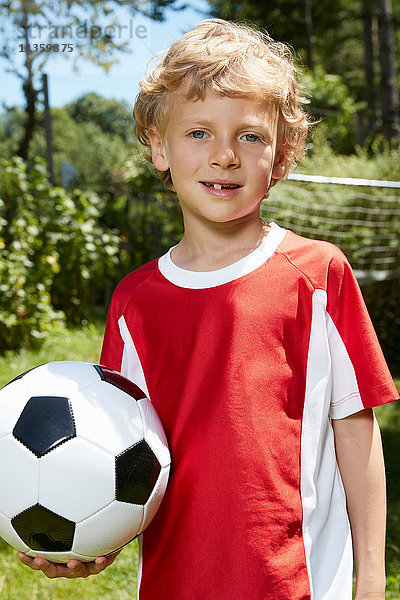 Nahaufnahme eines Jungen in Fussballuniform  der im Garten einen Fussball hält