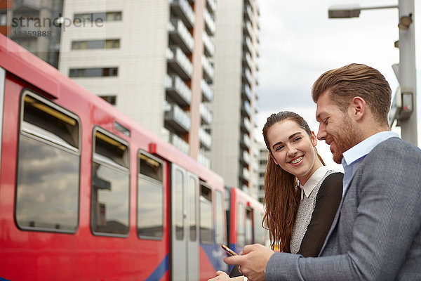 Geschäftsmann und Frau beim Lesen von Smartphone-Texten auf dem Bahnsteig  London  UK