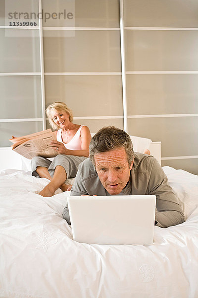 Paar auf dem Bett Zeitung lesen und mit Laptop