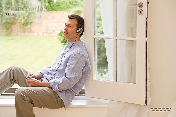 Erwachsener Mann hört Kopfhörermusik an der Terrassentür
