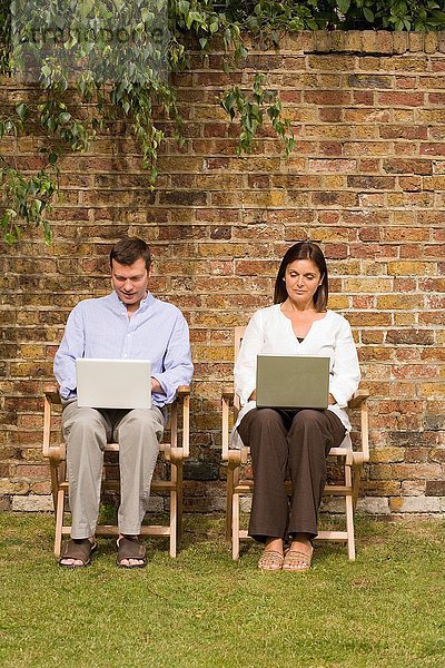 Reife Paare sitzen im Garten mit Laptops