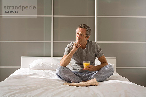 Verwirrter älterer Mann sitzend im Kreuzbein auf Bett mit Hand am Kinn