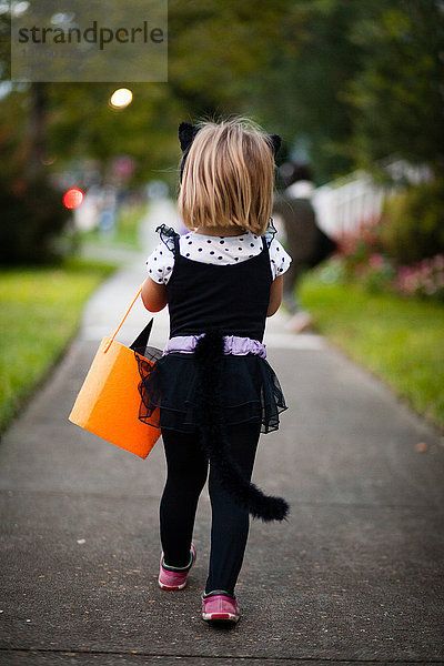 Rückansicht eines Mädchens  das im Katzenkostüm den Bürgersteig entlang läuft  bei Trick oder Behandlung