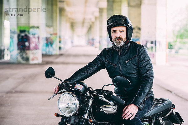 Erwachsener Motorradfahrer sitzt auf dem Motorrad und trägt einen Sturzhelm unter der Überführung.