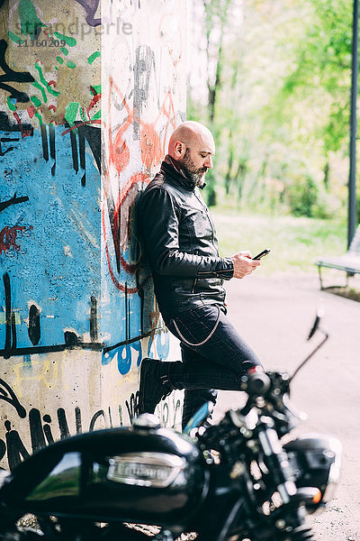 Reife Motorradfahrer lehnen sich an die Wand und lesen Smartphone-Texte.