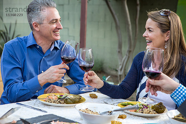 Ältere Freunde stoßen mit Rotwein am Tisch der Gartenparty an