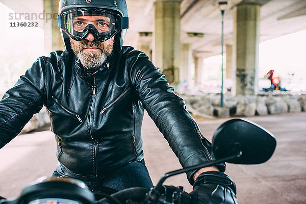 Erwachsener Motorradfahrer mit schwarzem Helm und Schutzbrille auf dem Motorrad unter der Überführung.