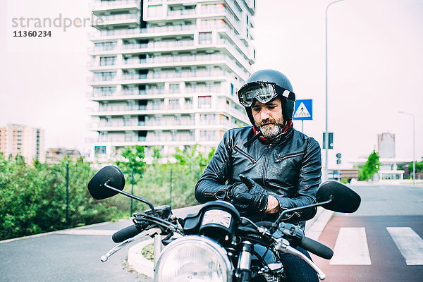 Erwachsener Motorradfahrer auf dem Motorrad sitzend  Handschuhe anziehend