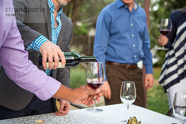 Männerhände gießen Rotwein am Tisch der Gartenparty
