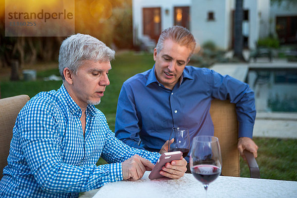 Zwei reife Männer benutzen ein Smartphone am Gartenparty-Tisch
