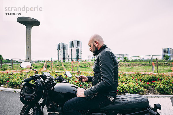 Erwachsener Motorradfahrer sitzt auf dem Motorrad und liest Smartphone-Text.