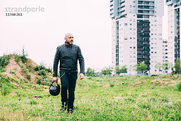 Erwachsener Motorradfahrer  der auf einem Brachland läuft und einen Helm trägt