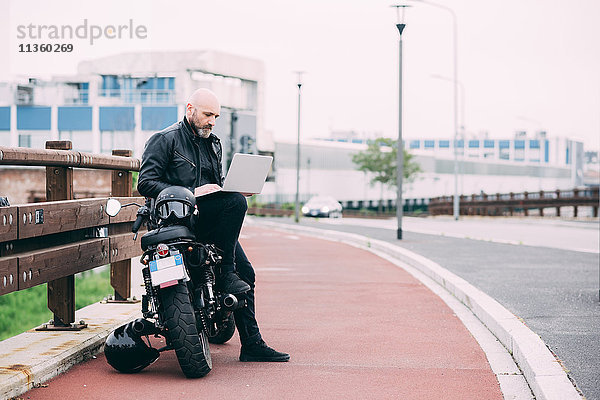 Erwachsener Motorradfahrer am Straßenrand mit Laptop