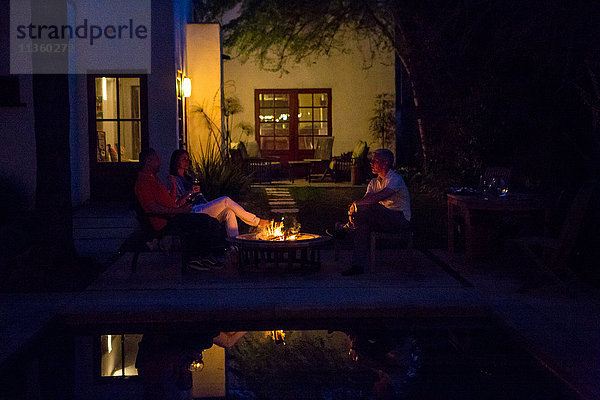 Reife Erwachsene entspannen sich in der Abenddämmerung am Terrassenfeuer