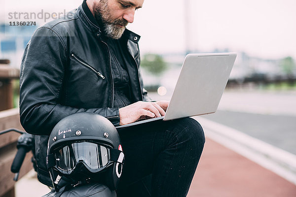 Erwachsener Motorradfahrer am Straßenrand mit Laptop